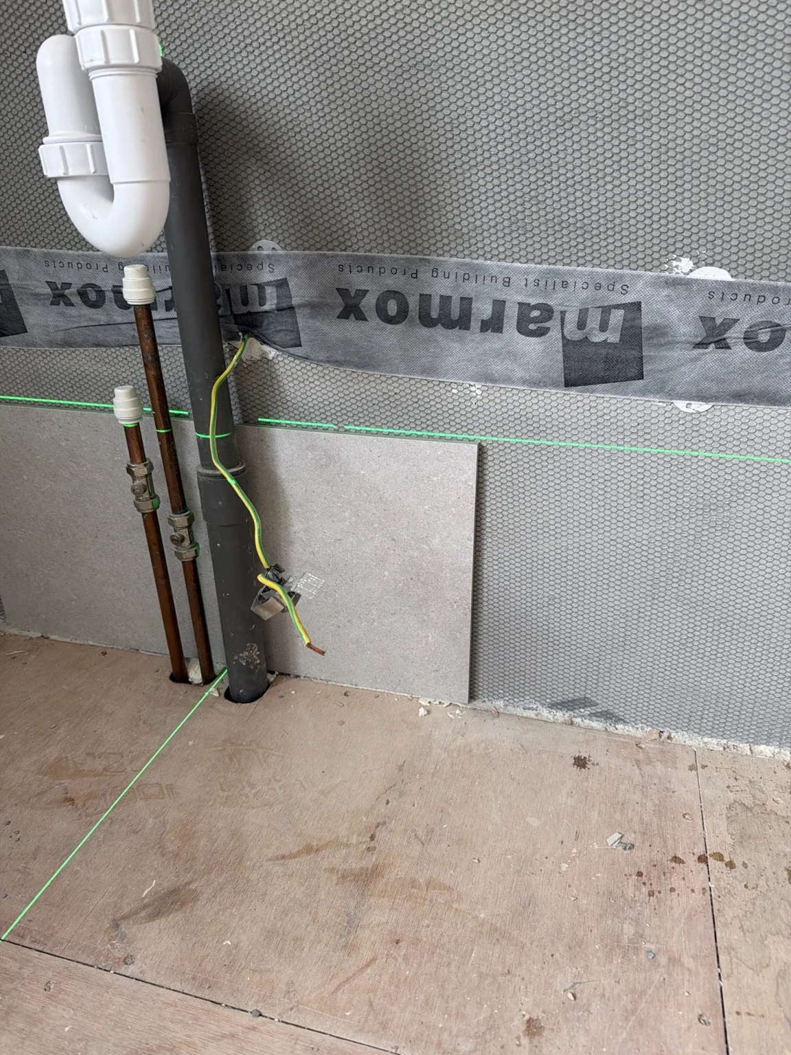 Marmox boards with sealed joints behind exposed basin pipework and waste.